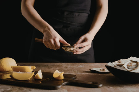 A person in a black apron squeezing lemon juice over oysters on a table.