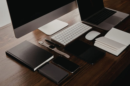 A modern workspace with a computer, laptop, keyboard, mouse, notebook, and various electronic...