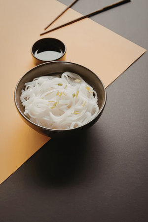 A bowl of white noodles with green onions and a small bowl of sauce, accompanied by chopsticks.