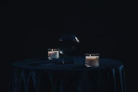 The image depicts a round table with a dark blue velvet cover, adorned with two lit candles in glass...