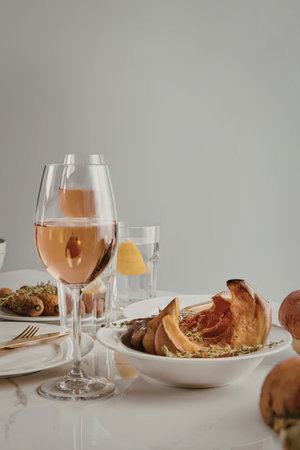 A wine glass and a plate of food on a white table with a bowl of food and a glass of water
