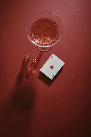 A still life image featuring a glass of red drink, a playing card with a heart suit, and two red...