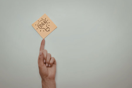 A hand is holding up a sticky note with a simple drawing of a lightbulb, symbolizing an idea or inspiration.の写真素材