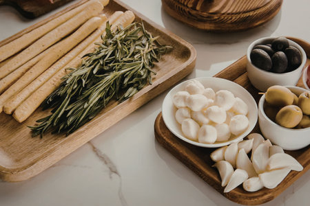 a close-up of wooden trays holding breadsticks, herbs, mozzarella balls, and olivesの写真素材