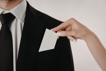 A close-up image of a man's suit with a hand holding a blank white business card near his chest...