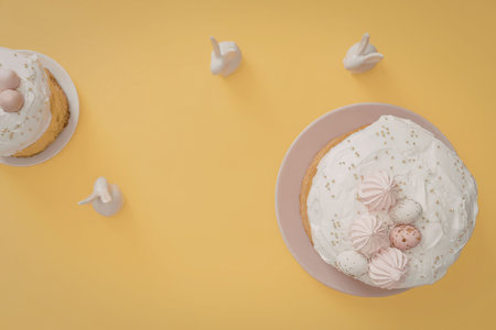 Two cakes with white frosting are placed on a yellow background, one on a plate and the other on a...