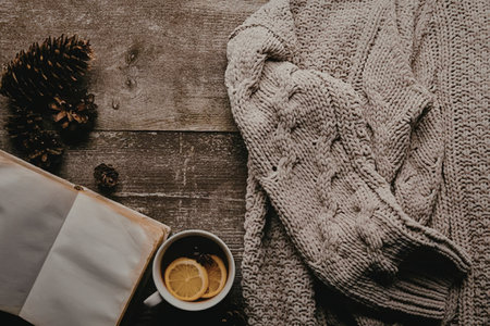 A cup of tea, a book and a sweater on a wooden table