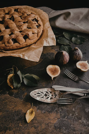A beautifully presented fig pie with a lattice crust, accompanied by fresh figs, leaves, and...