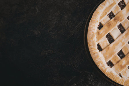 A close-up of a homemade lattice pie on a dark background, showcasing its golden-brown crust and...