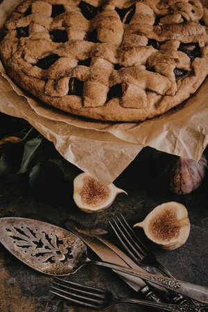 A beautifully presented fig pie with a lattice crust, accompanied by sliced figs and utensils,...