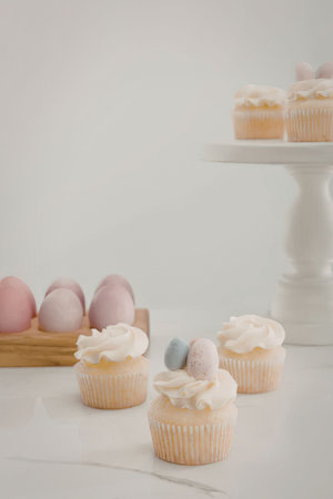 A close-up of cupcakes with white frosting and decorative eggs on top, with a wooden tray of pink...