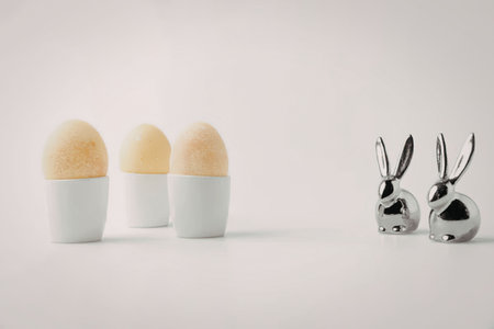 A set of white and yellow egg holders alongside shiny metal bunny figurines