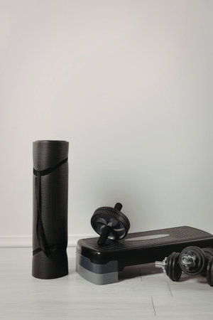 A yoga mat, step platform, and dumbbells on a white wooden floor.