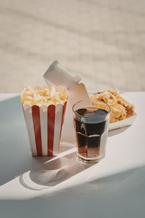 a glass of soda, a bucket of french fries and a plate of fried chicken on a white table