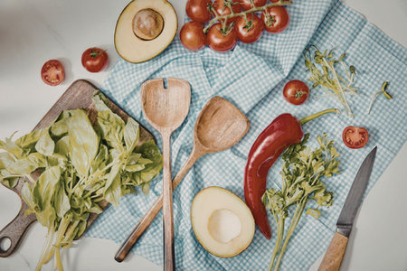 A kitchen towel with fresh vegetables and fruits, including avocado, tomatoes, pepper, and leafy...