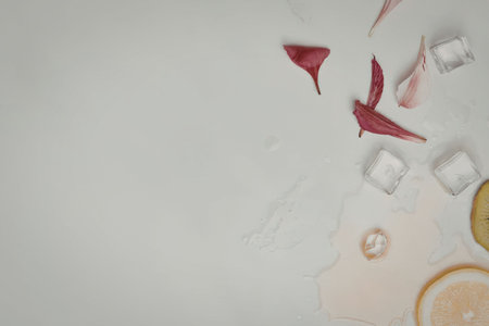 A refreshing summer drink setup with ice cubes and rose petals on a white surface.