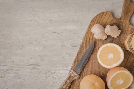 A wooden cutting board with sliced oranges, whole ginger, and a knife on a marble countertopの写真素材