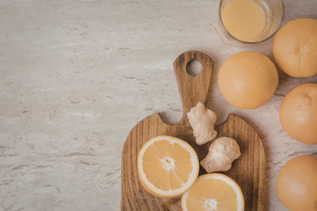 A wooden cutting board with sliced oranges and ginger, accompanied by whole oranges and a glass of...