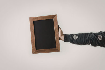 A hand in a dark green sleeve holding a small, blank blackboard against a white background.