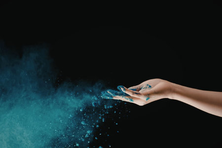 A hand releasing blue particles into the air on a black backgroundの写真素材