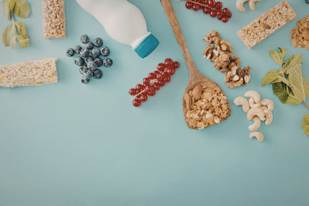 A selection of healthy food ingredients including nuts, seeds, dried fruits, and milk on a blue...