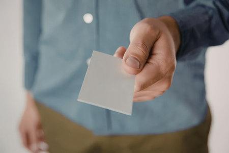 A man in a blue shirt holding a blank white business card in his hand.