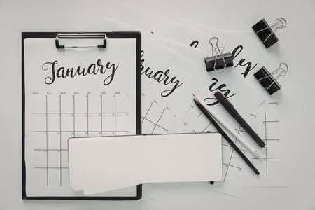 A clipboard with a January calendar, blank cards, and office supplies like binder clips and pens.