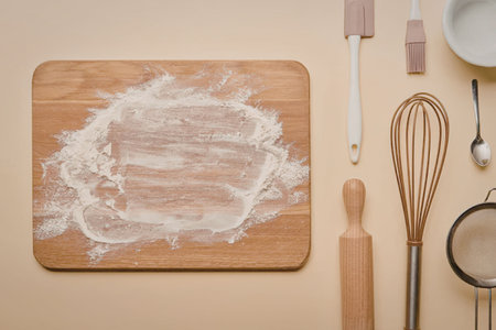 A wooden cutting board with flour on it and various kitchen utensils arranged around it.