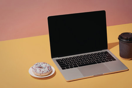 A laptop, donut and coffee cup on an orange table with pink wall