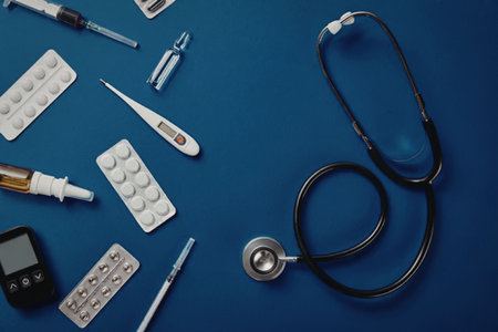 A stethoscope and various medical supplies, including pills, thermometer, and syringe, are arranged...