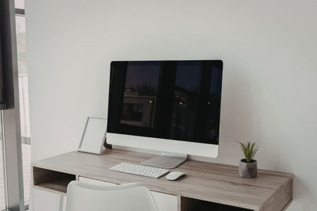 A modern home office setup with a computer monitor, keyboard, mouse, and a small plant on a wooden...