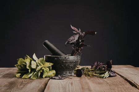 A mortar and pestle with fresh herbs on a wooden table against a dark background