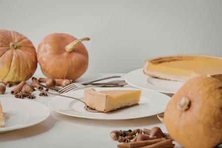 A table setting with a slice of pumpkin pie on a plate, surrounded by whole pumpkins, nuts, and...
