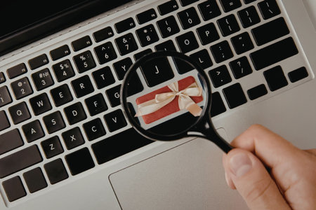 A hand holding a magnifying glass over a laptop keyboard