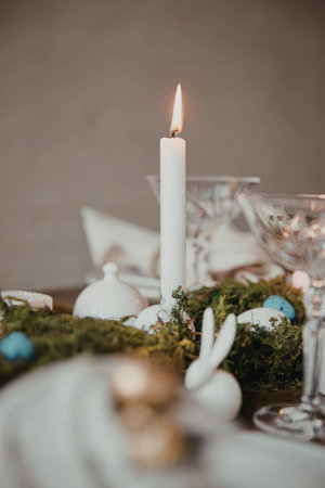A serene Easter table setting featuring a lit white candle, surrounded by lush greenery, white and...