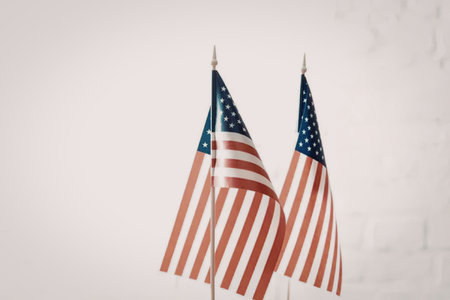 Two small American flags waving side by side against a white background, symbolizing patriotism and...