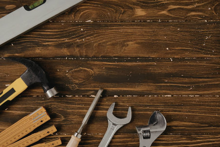 A selection of tools including a hammer, screwdriver, wrenches, and pencils on a dark wooden...