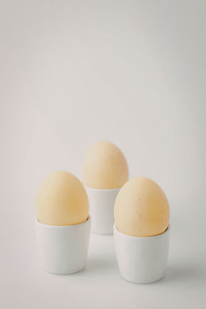 Three yellow eggs in white cups on a plain white background