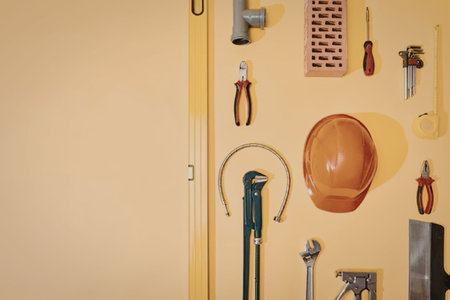 A collection of various tools hanging on a yellow wall, including a hard hat, pliers, screwdrivers,...
