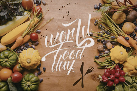 A vibrant arrangement of fresh vegetables and fruits on a wooden table with the text 'world food day' in white cursive fontの写真素材