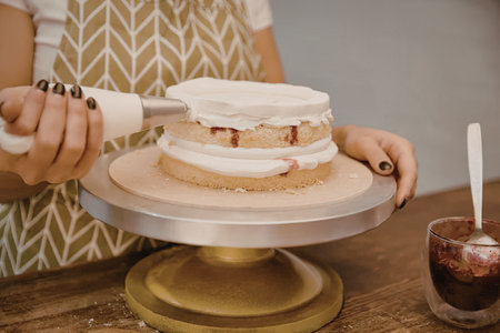 A woman in an apron frosting a layered cake with white icing