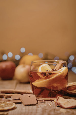 A glass of warm spiced cider with orange slices and cinnamon sticks, accompanied by chocolate pieces...