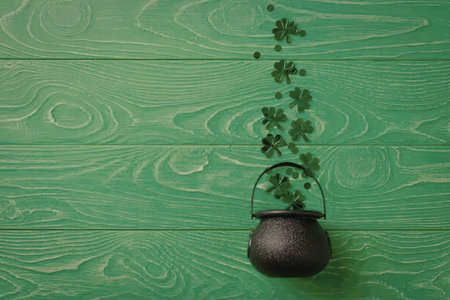 Black cauldron sits on vibrant green wooden background with shamrocks falling into it symbolizing...
