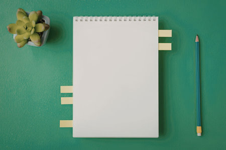 Blank spiral notebook with yellow sticky notes and a pencil on a green background accompanied by a...