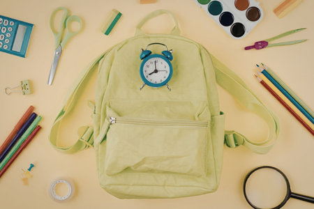 Bright green backpack surrounded by school supplies like colored pencils scissors and paint on a...