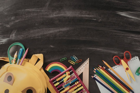 Colorful school supplies including a yellow backpack and various learning tools are arranged on a...