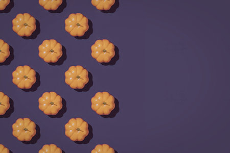 Small bright orange artificial pumpkins are arranged in a diagonal pattern on a vibrant purple...