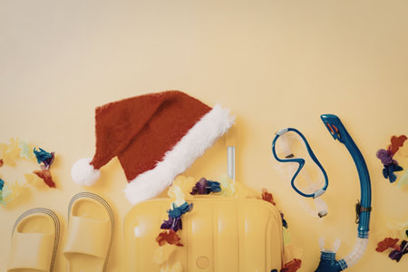 Yellow suitcase filled with beach accessories and santa hat on bright yellow background symbolizing...