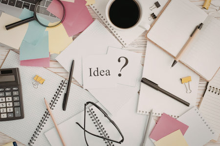 Cluttered desk with scattered stationery supplies and a note that says idea question mark surrounded...