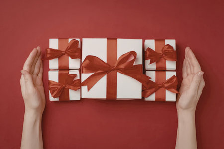 Hands carefully holding white gift boxes with red ribbons and bows on a vibrant red background...